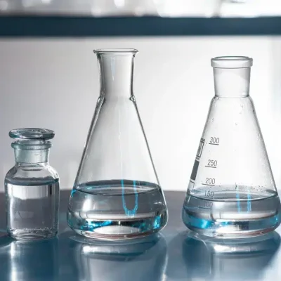 close-up of a clear liquid being poured into a laboratory glass beaker or flask, representing industrial hydrosol chemical production.